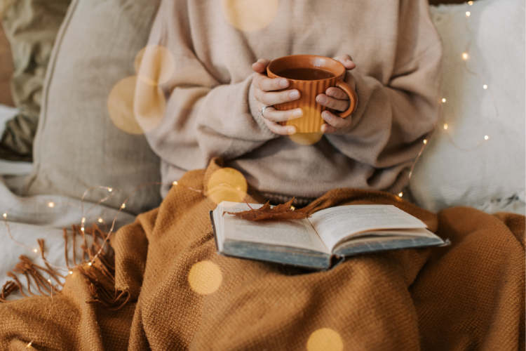In der Übergangszeit gibt es verschiedene Methoden zu heizen (Frau mit Decke am Buch lesen und Tee trinken)