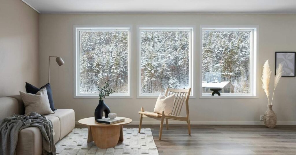 Helles wohnzimmer mit sofa, sessel und couchtisch. Grosse fenster bieten einen blick auf einen verschneiten wald. Trockene raumluft im winter.